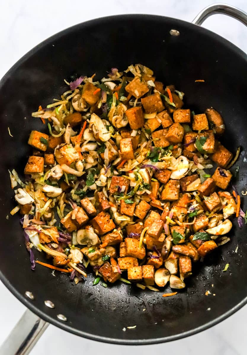 Black round pan filled with sautéed veggies and crispy tofu.