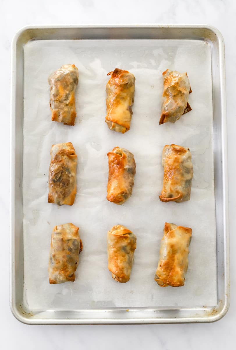 Baking sheet lined with parchment paper with 9 crispy baked filled rolls on it.