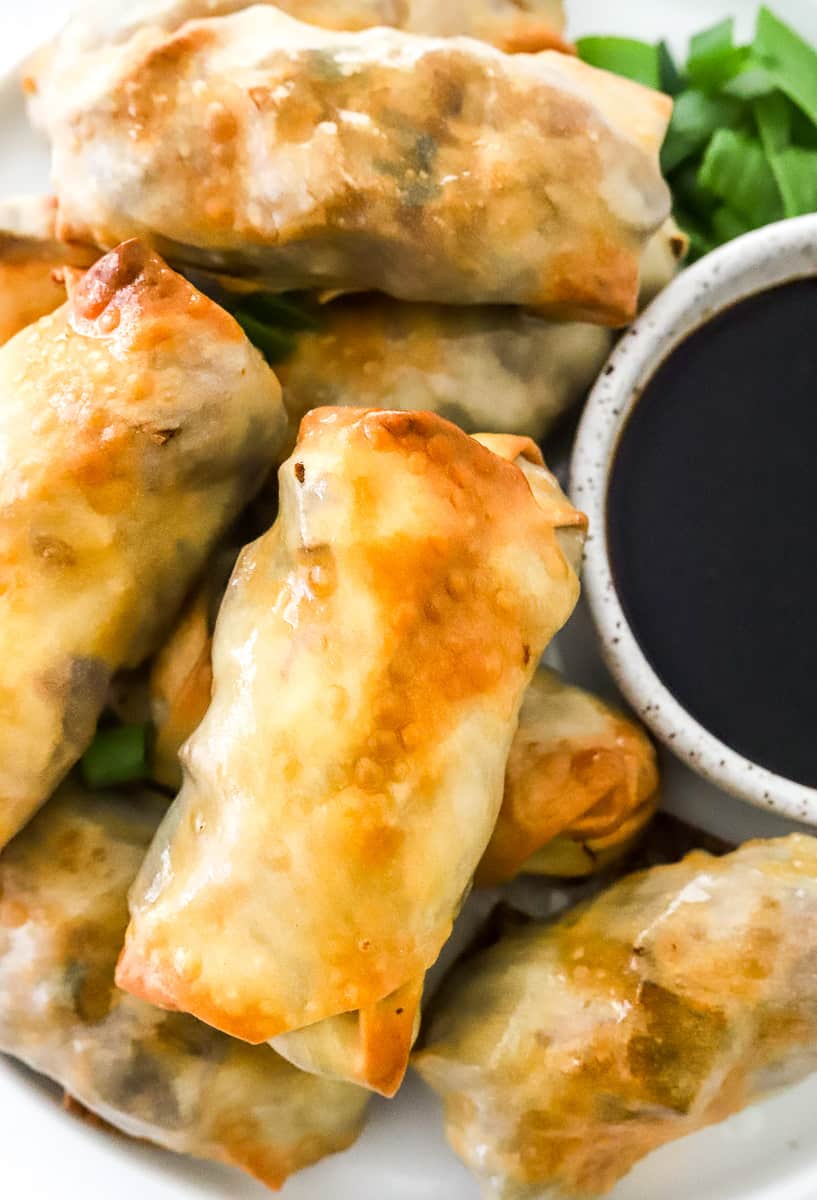 A few crispy baked egg rolls on a plate with a bowl of soy sauce.