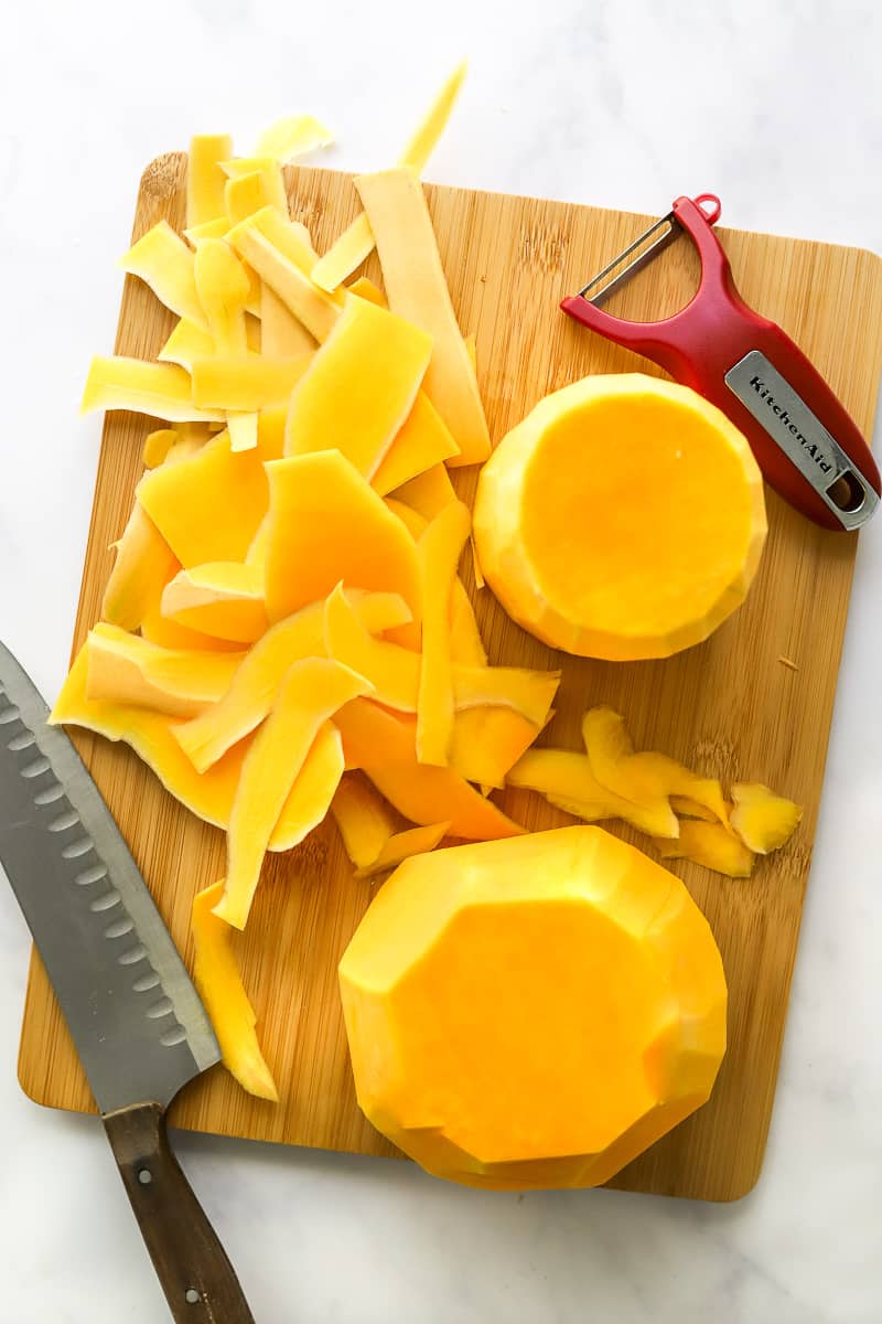 Peeled halves of butternut squash on a wooden cutting board.