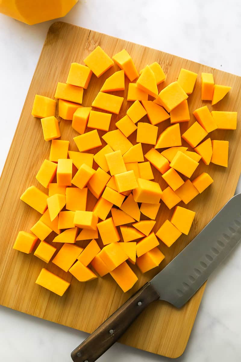 Cubed butternut squash on a brown cutting board with a knife next to it. 