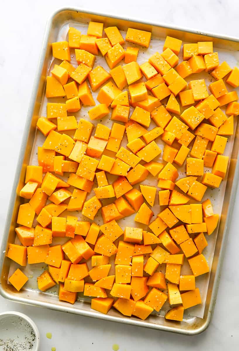 Cubed, seasoned uncooked squash on a baking sheet. 