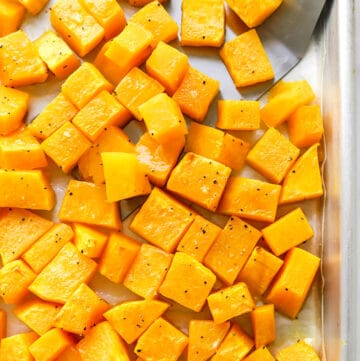 Cubed roasted butternut squash on a baking sheet with a silver spatula on it.