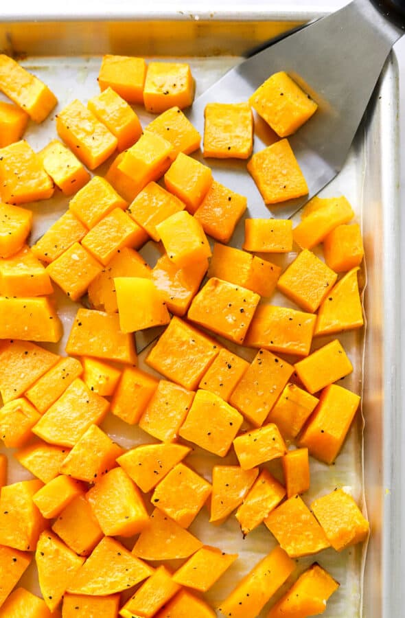 Cubed roasted butternut squash on a baking sheet with a silver spatula on it.