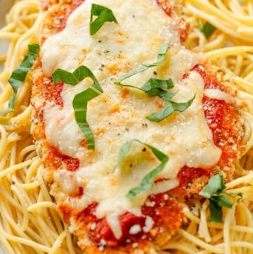 Baked gluten free chicken parmesan on top of cooked pasta on a plate.