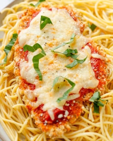 Baked gluten free chicken parmesan on top of cooked pasta on a plate.