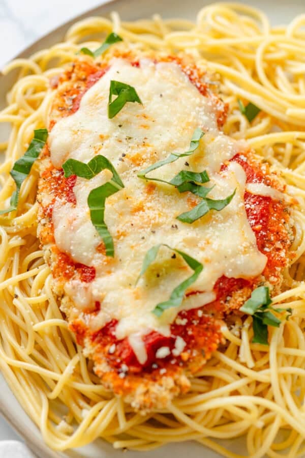 Baked gluten free chicken parmesan on top of cooked pasta on a plate.