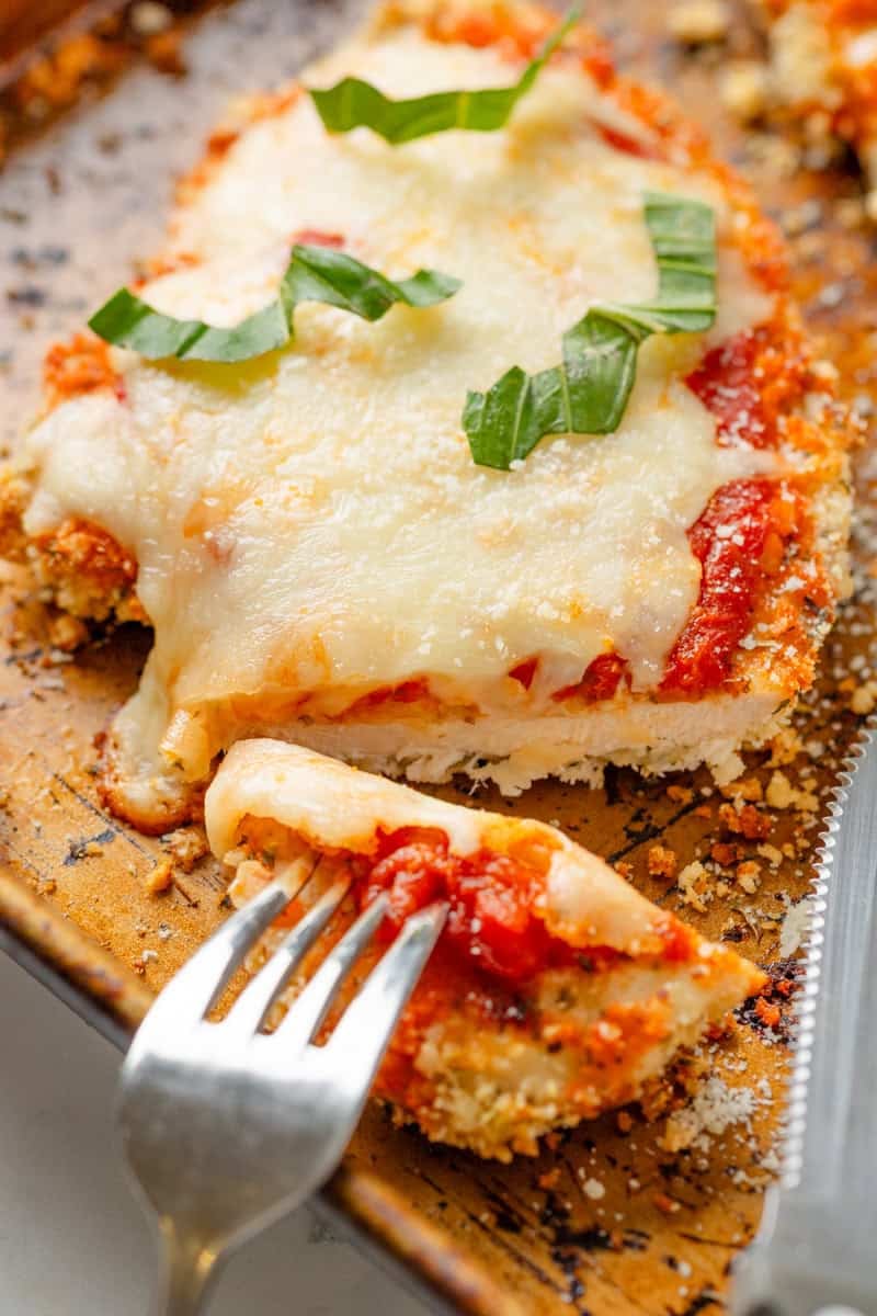 Breaded cooked chicken with sauce and melty cheese on a baking a with a cut out of it. 