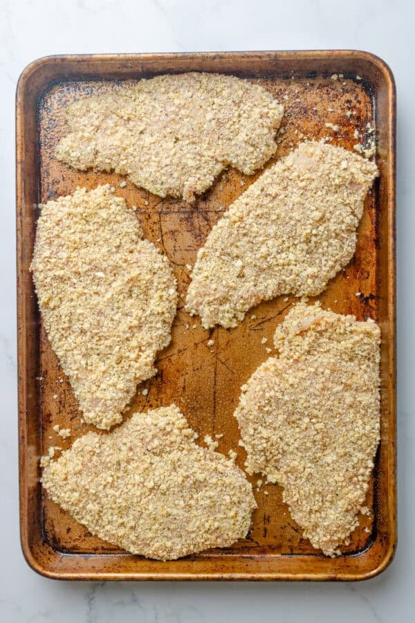 Uncooked coated chicken cutlets on baking pan.