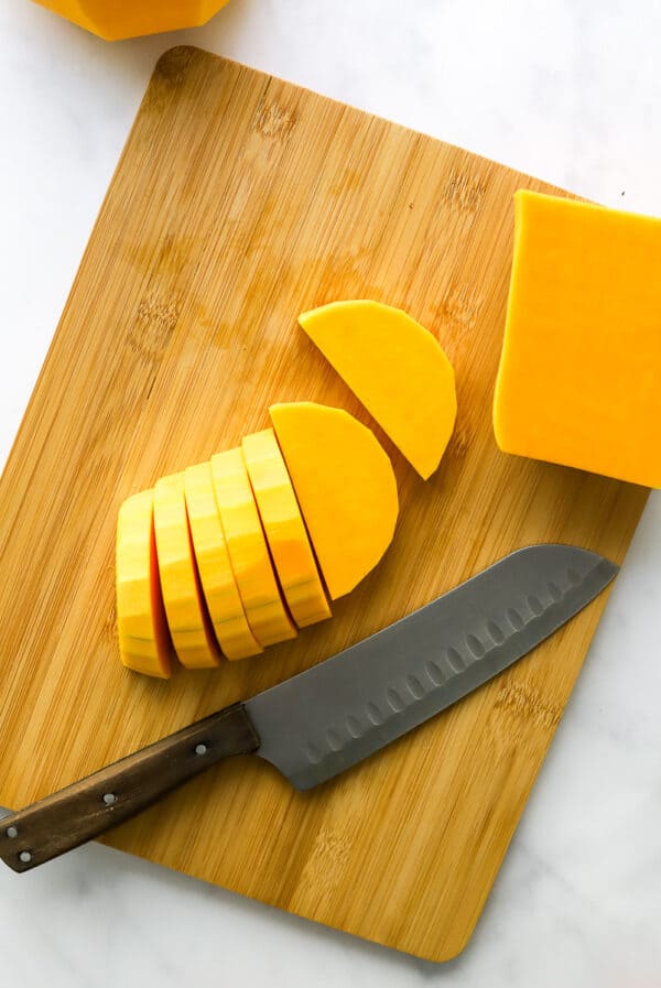 Sliced half moons of butternut squash on a wood board with a knife on the board.