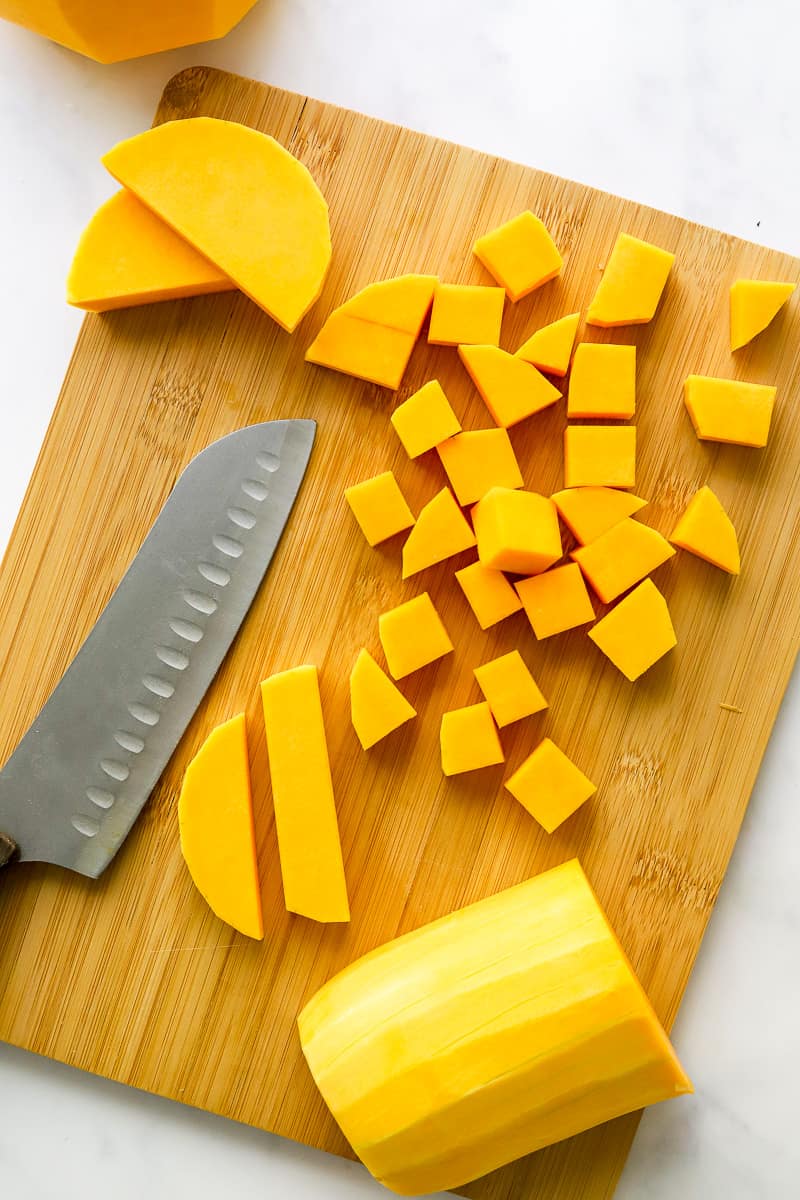 Cubes of squash and some whole, peeled squash on a cutting board with a knife on the board next to it.