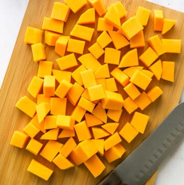 Cubed butternut squash on a cutting board with a knife on the board in front of it.