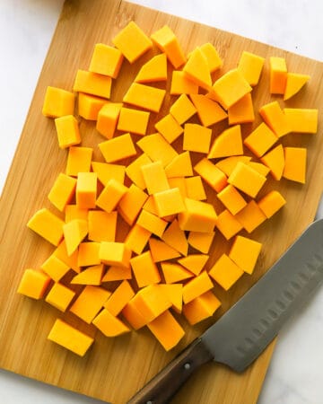 Cubed butternut squash on a cutting board with a knife on the board in front of it.