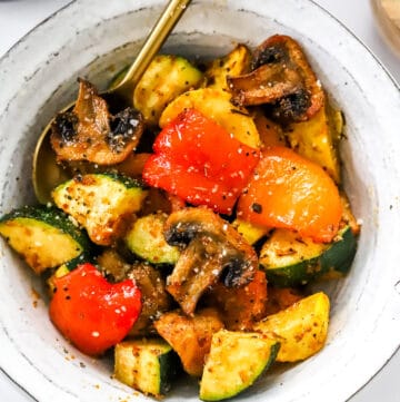 Roasted zucchini, squash, mushrooms and peppers in a round bowl with a spoon in the bowl.