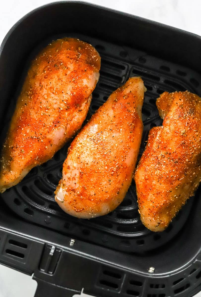 3 uncooked seasoned chicken breasts in a square air fryer basket.