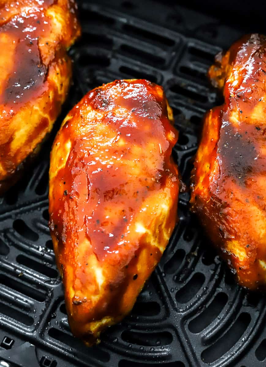 Cooked chicken breasts covered in bbq sauce in a black air fryer.