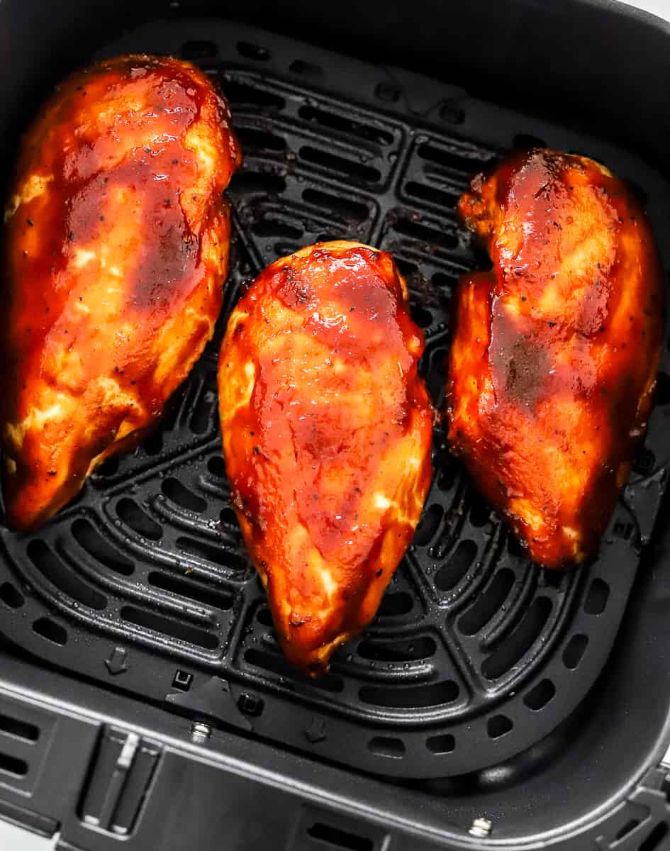 3 bbq coated chicken breasts in a square, black air fryer basket.