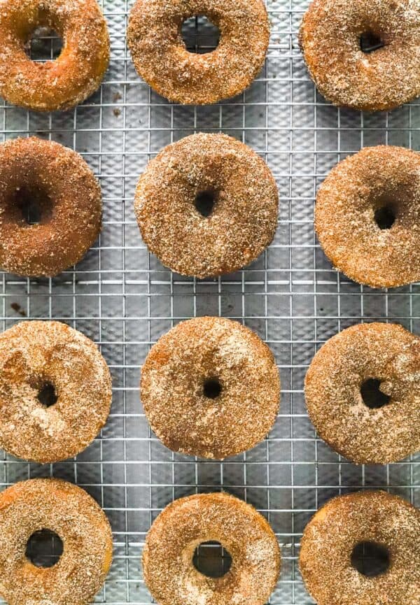 A bunch of baked, sugar coated brown donuts on a rack on a baking sheet.