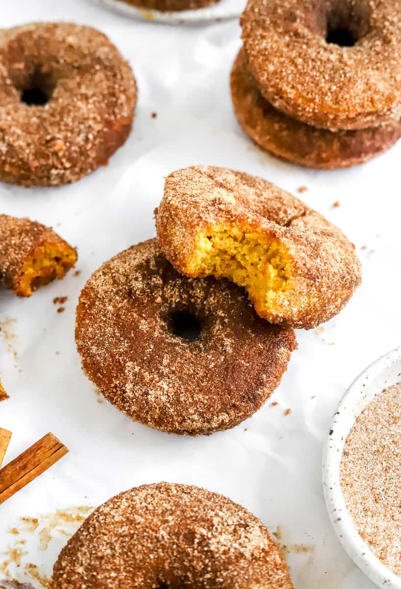 Golden brown donut covered in cinnamon sugar with another donut with a bite out of it on top of it and more donuts around it.