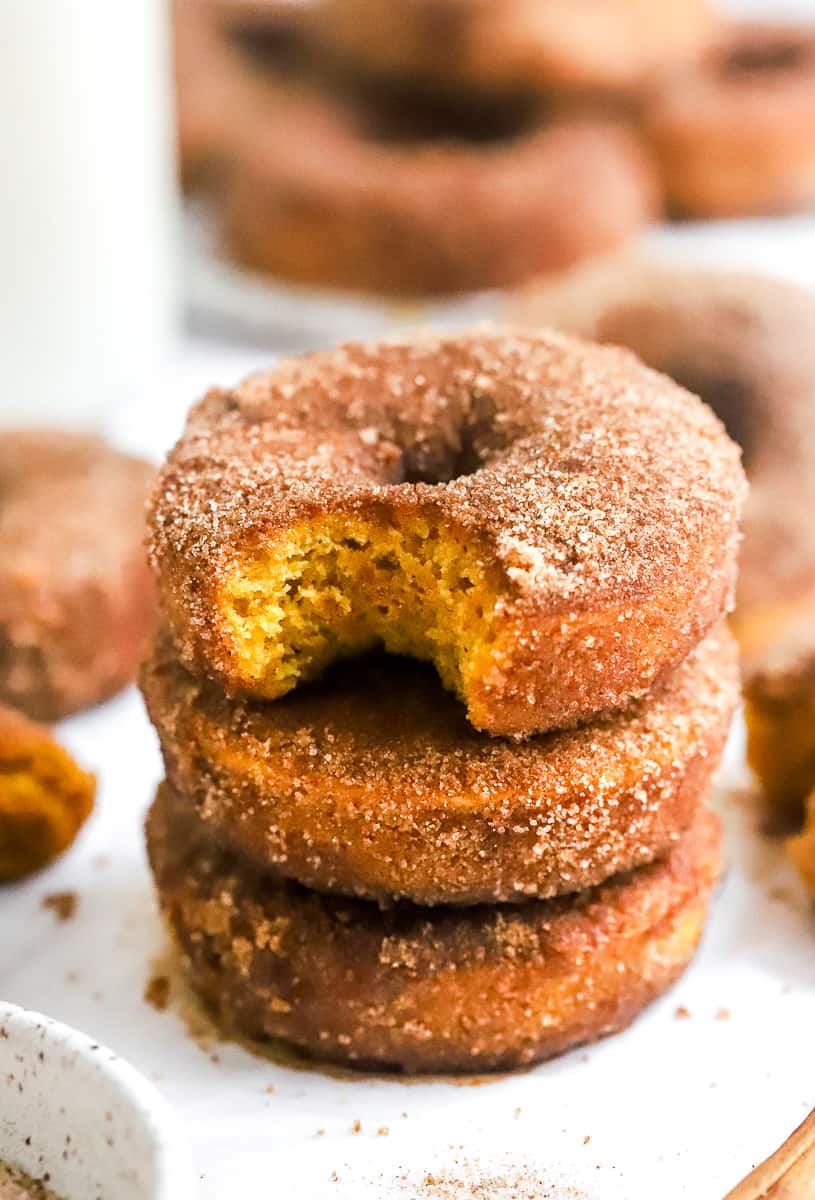 Close up of 3 pumpkin spice donuts stacked on top of one another with more donut behind them.