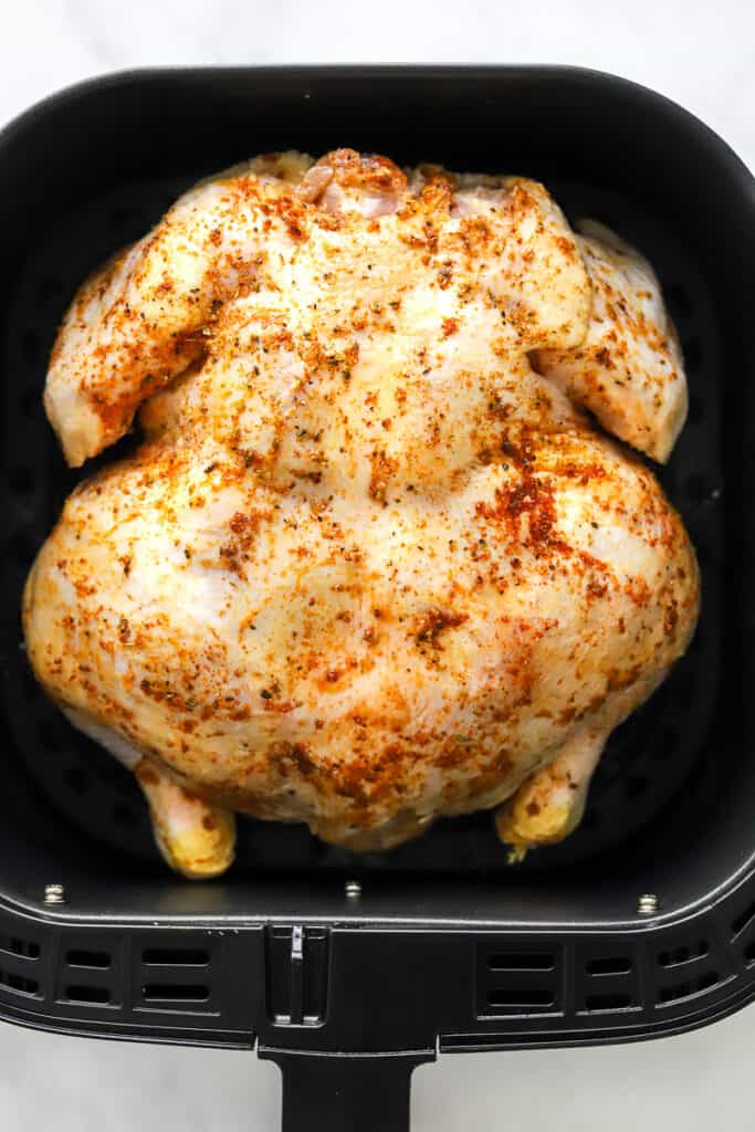 Seasoned, uncooked whole chicken in an air fryer basket.