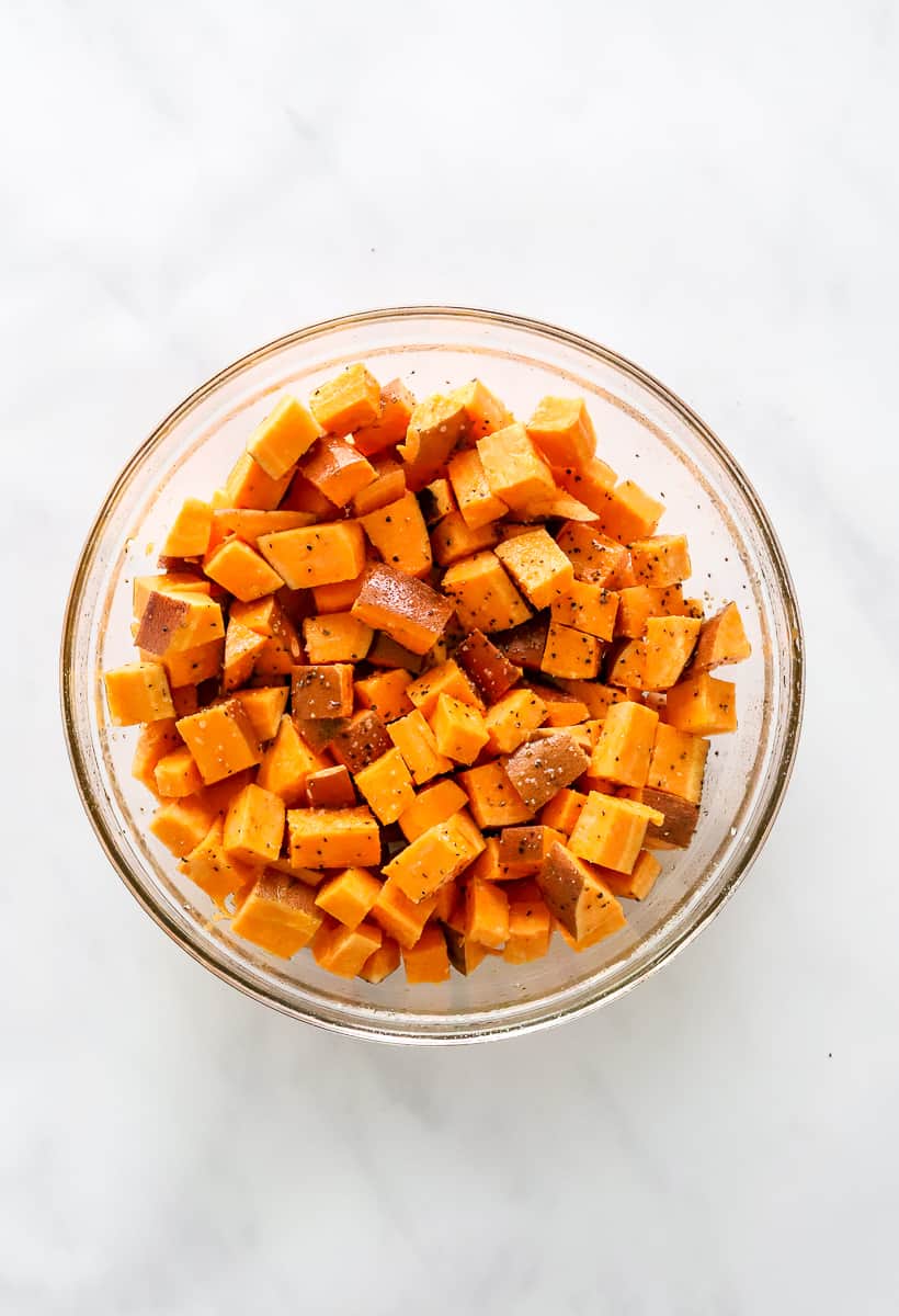 Chopped raw sweet potatoes in a bowl topped with salt and pepper.