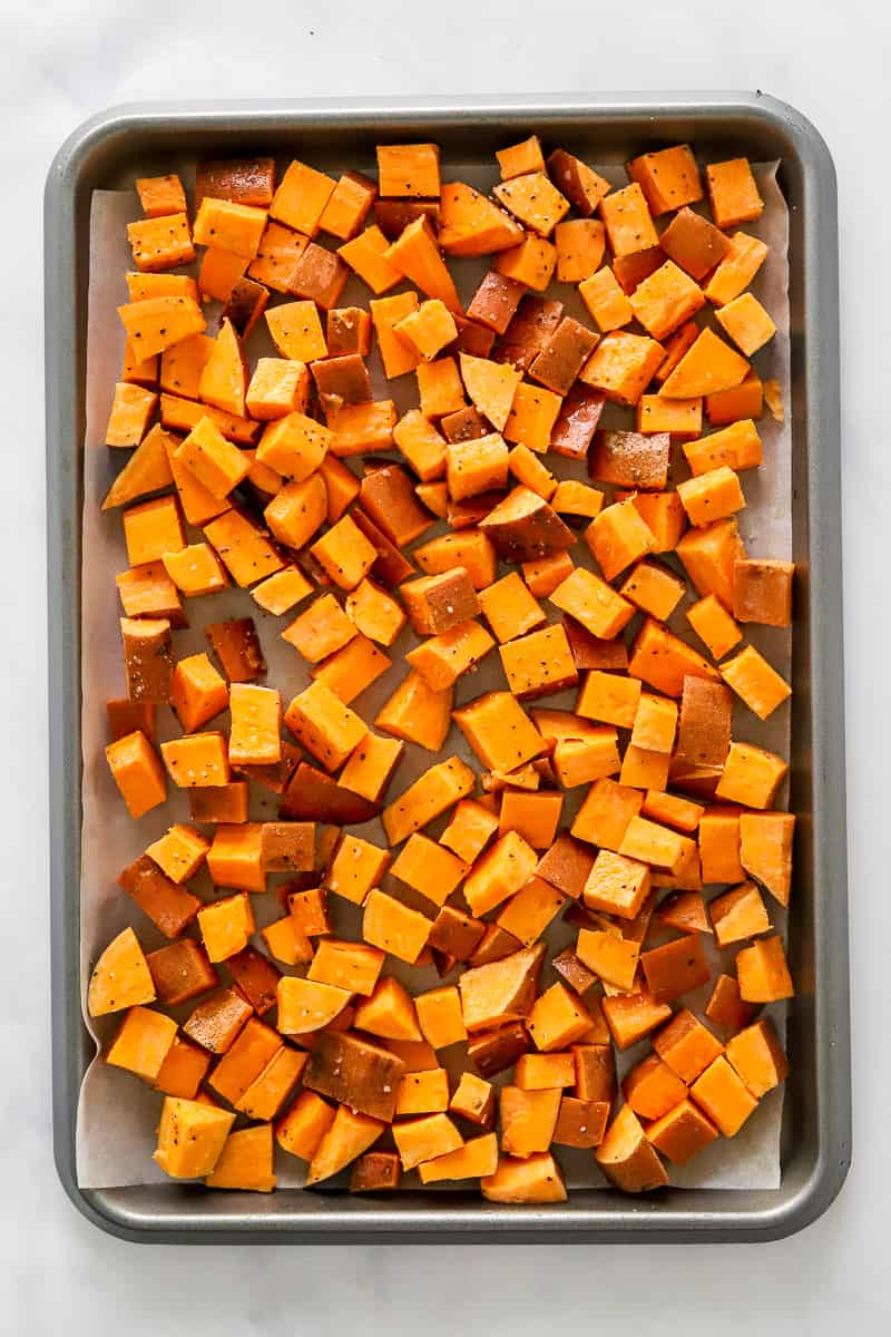 Seasoned, chopped raw sweet potatoes on a baking sheet.