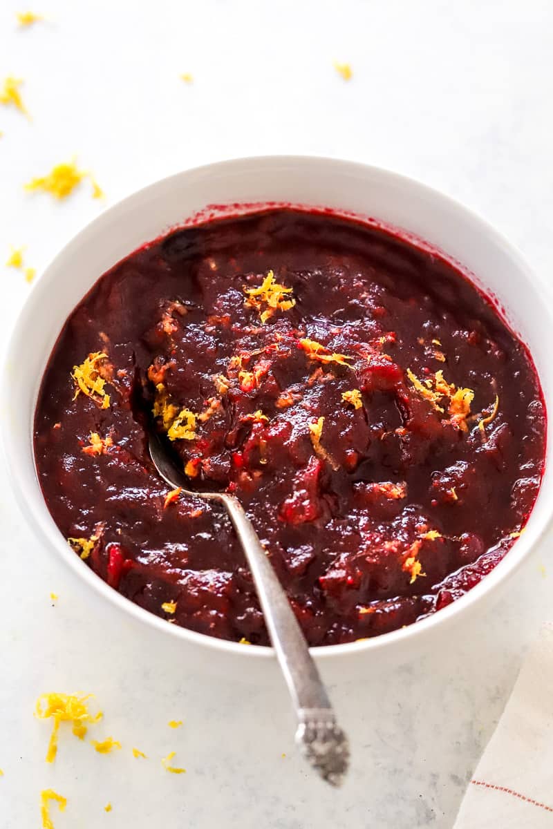 Mixed cranberry sauce in a bowl garnished with orange zest with a spoon in the bowl with the sauce. 