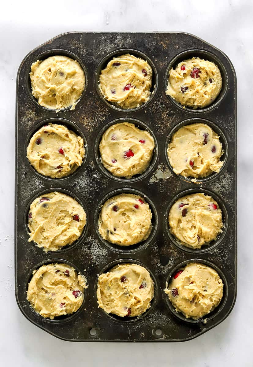 12 cup muffin pan filled with raw muffin batter with cranberries in it.