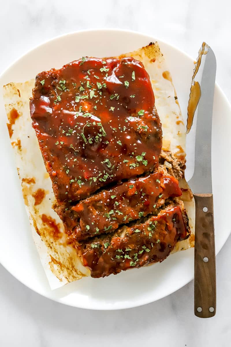 Cooked whole meatloaf sliced on a plate with a knife next to it.
