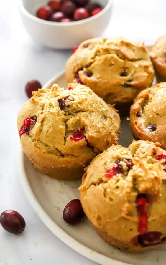Cranberry orange muffins on a plate with more cranberries next to them and in a bowl behind them.