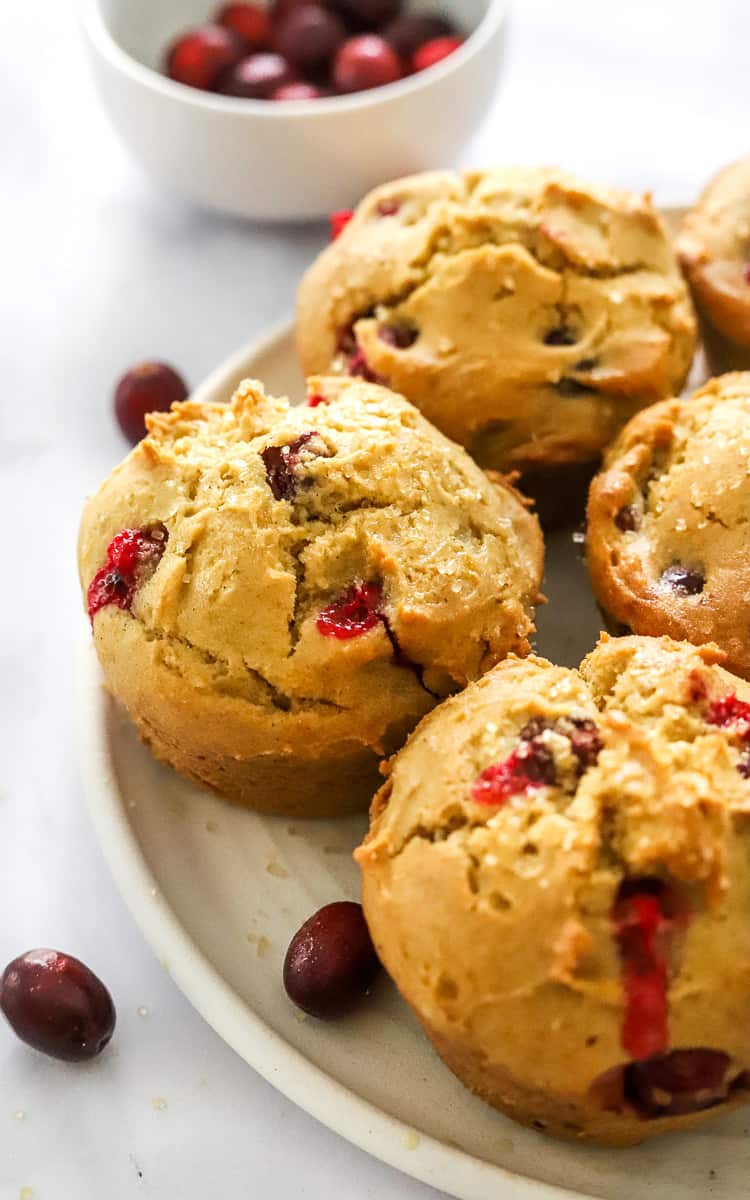 Cranberry orange muffins on a plate with more cranberries next to them and in a bowl behind them.