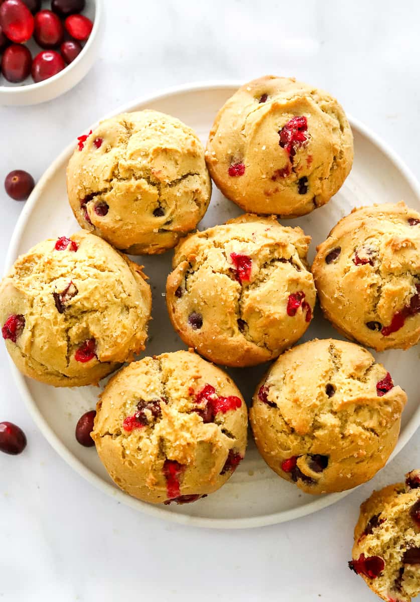 Plate of baked orange cranberry muffins with a bowl of whole fresh cranberries behind them.