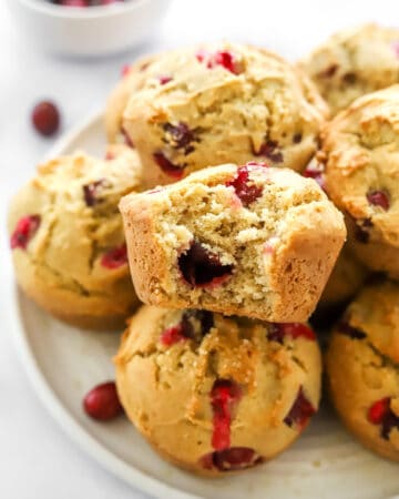 Baked muffins filled with cranberries on a plate with a bit taken on to one of the muffins.