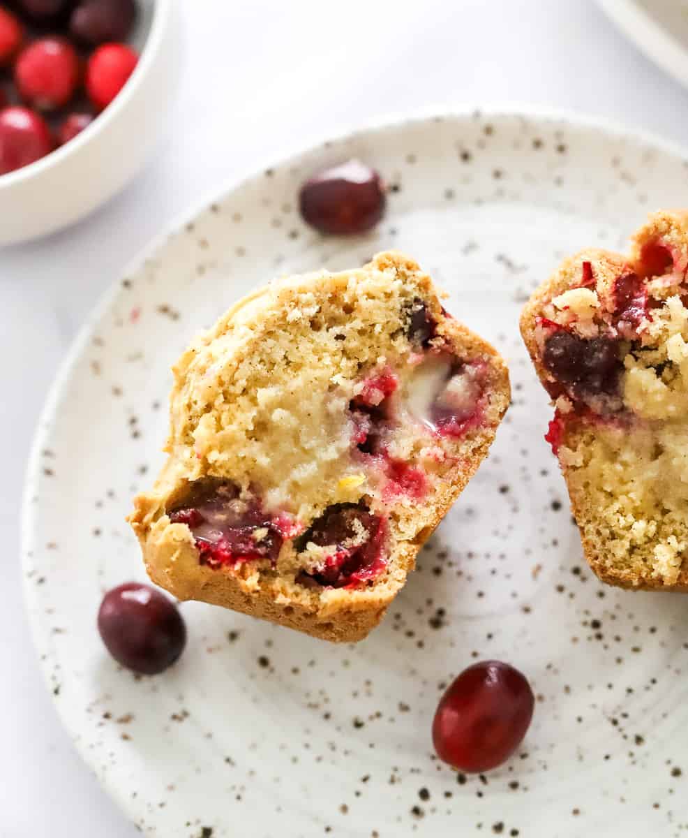 Cut muffin with red cranberries in it with butter slathered on it on a plate.
