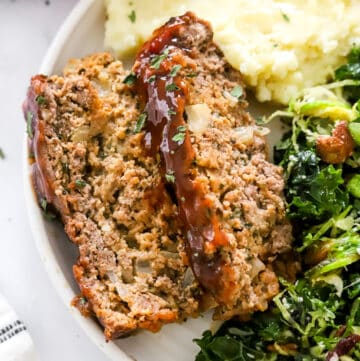 Two slices of gluten free meatloaf on a plate with mashed potatoes and salad.