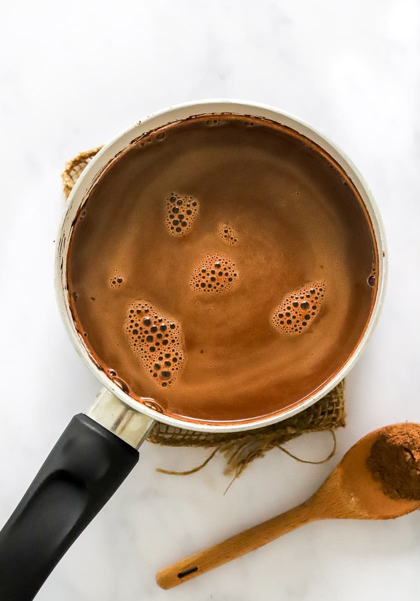 Vegan hot chocolate cooking in a small pot with more hot chocolate mix in a spoon next to it.