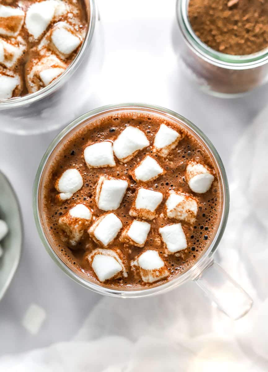 Mug of chocolate cocoa with lots marshmallows on top with another glass mug of it behind it.