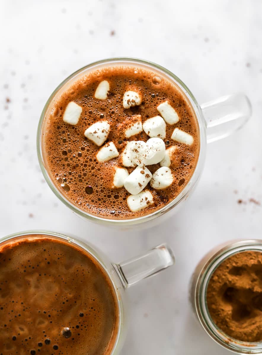 Glass mugs with vegan cocoa in them with small marshmallows on top of one of them.