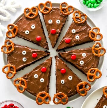 Round plate of decorated reindeer brownies with bowls of red and green candies around them.