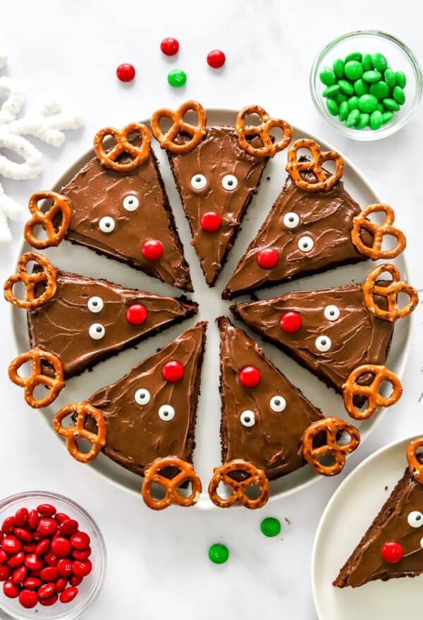 Round plate of decorated reindeer brownies with bowls of red and green candies around them.