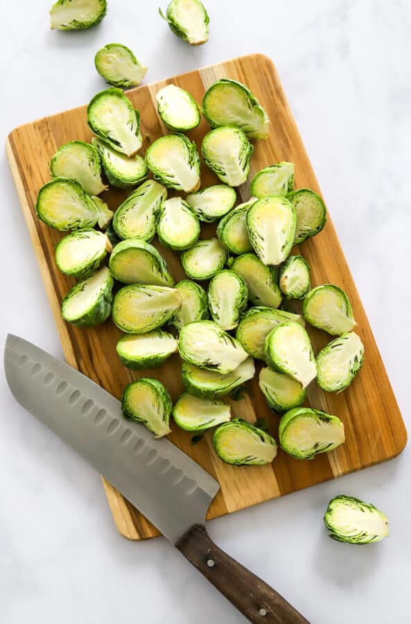 Sliced Brussels sprouts on a wood butting board with a knife on the board.