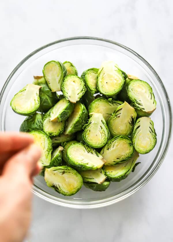 Sliced brusseles sprouts in a glass bowl with a hand seasoning them.