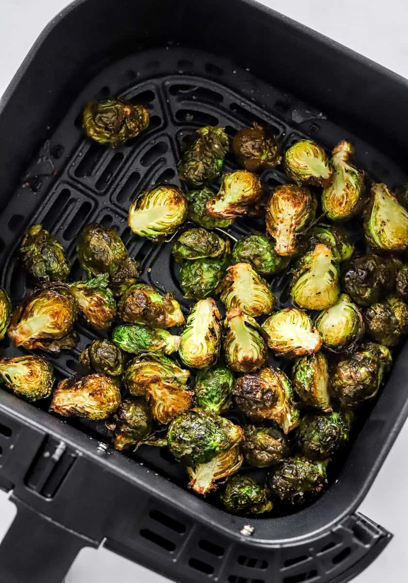 Cooked crispy Brussels sprouts in a black air fryer basket.