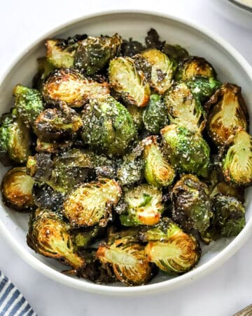 Cooked, sliced air fryer Brussels sprouts in a round bowl with grated parmesan cheese sprinkled on them.