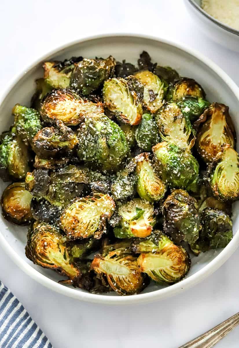 Cooked, sliced air fryer Brussels sprouts in a round bowl with grated parmesan cheese sprinkled on them.