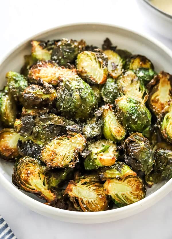 Bowl filled with crispy golden Brussels sprouts halves topped with parmesan cheese.