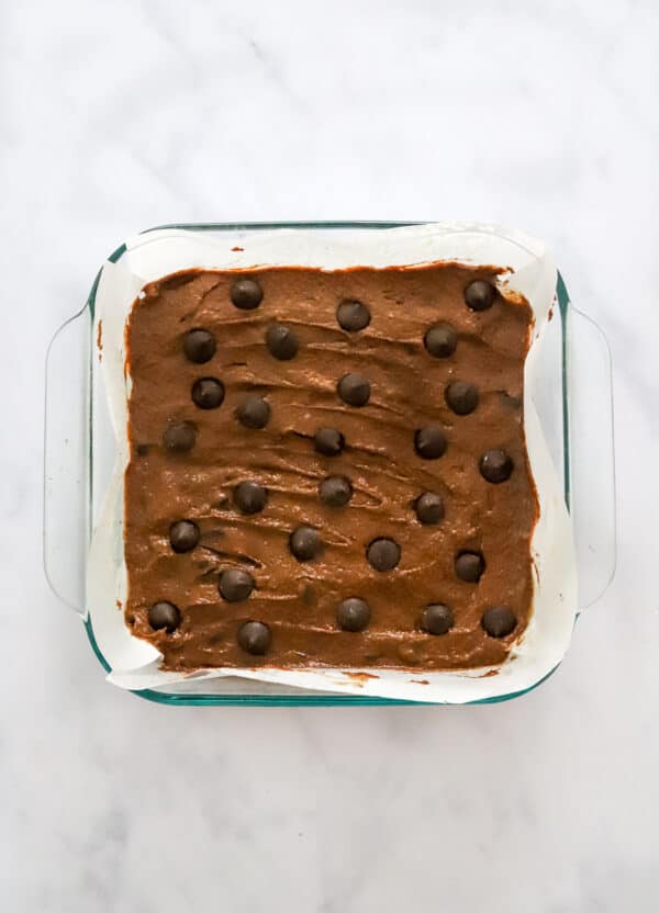 Uncooked brownie batter in a parchment lined pan.