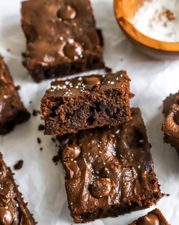 Brownie squares on white parchment pare with a wood bowl of salt behind them.