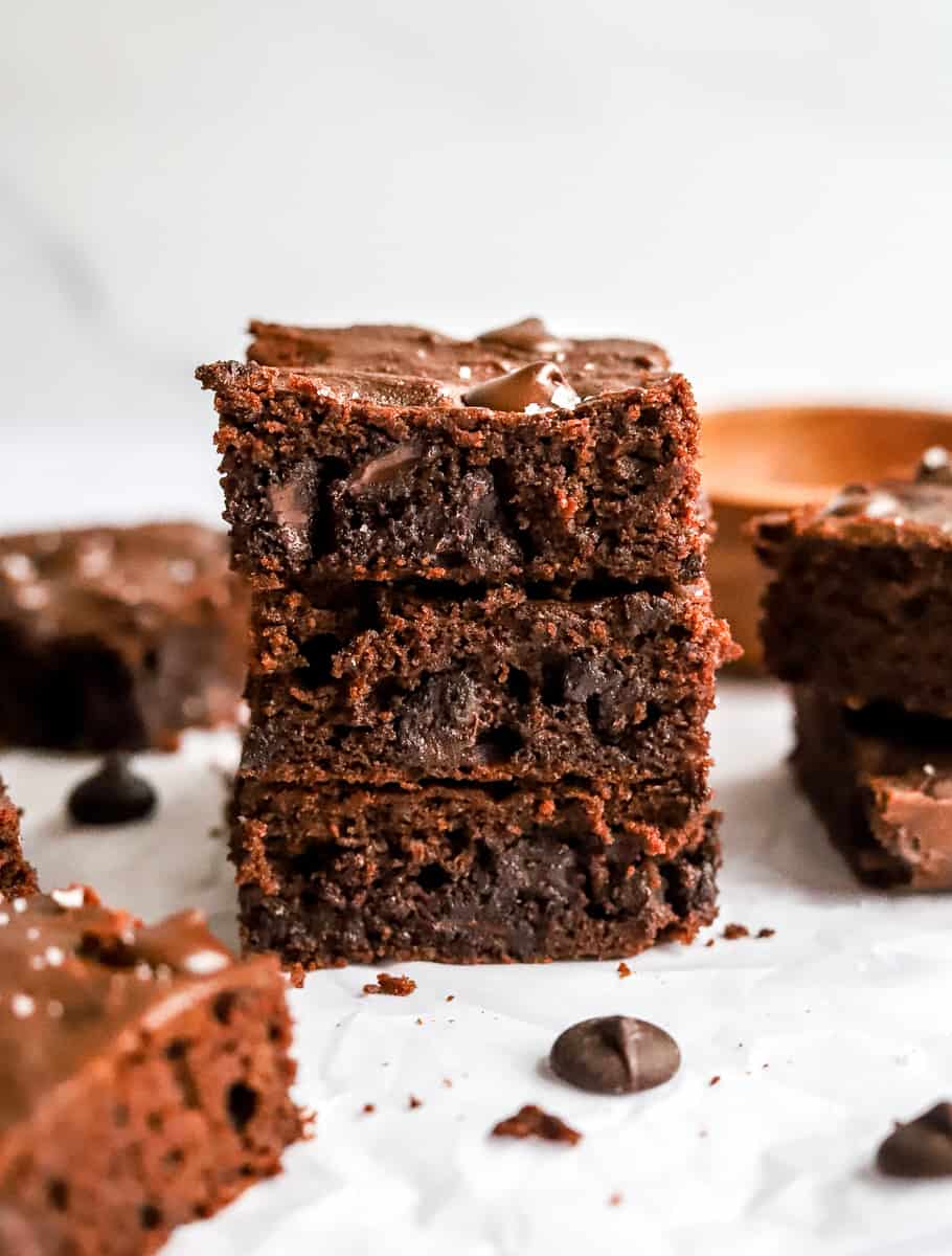 Stack of 3 healthy brownies that are chocolately and fudgy with more brownies next to and behind them. 